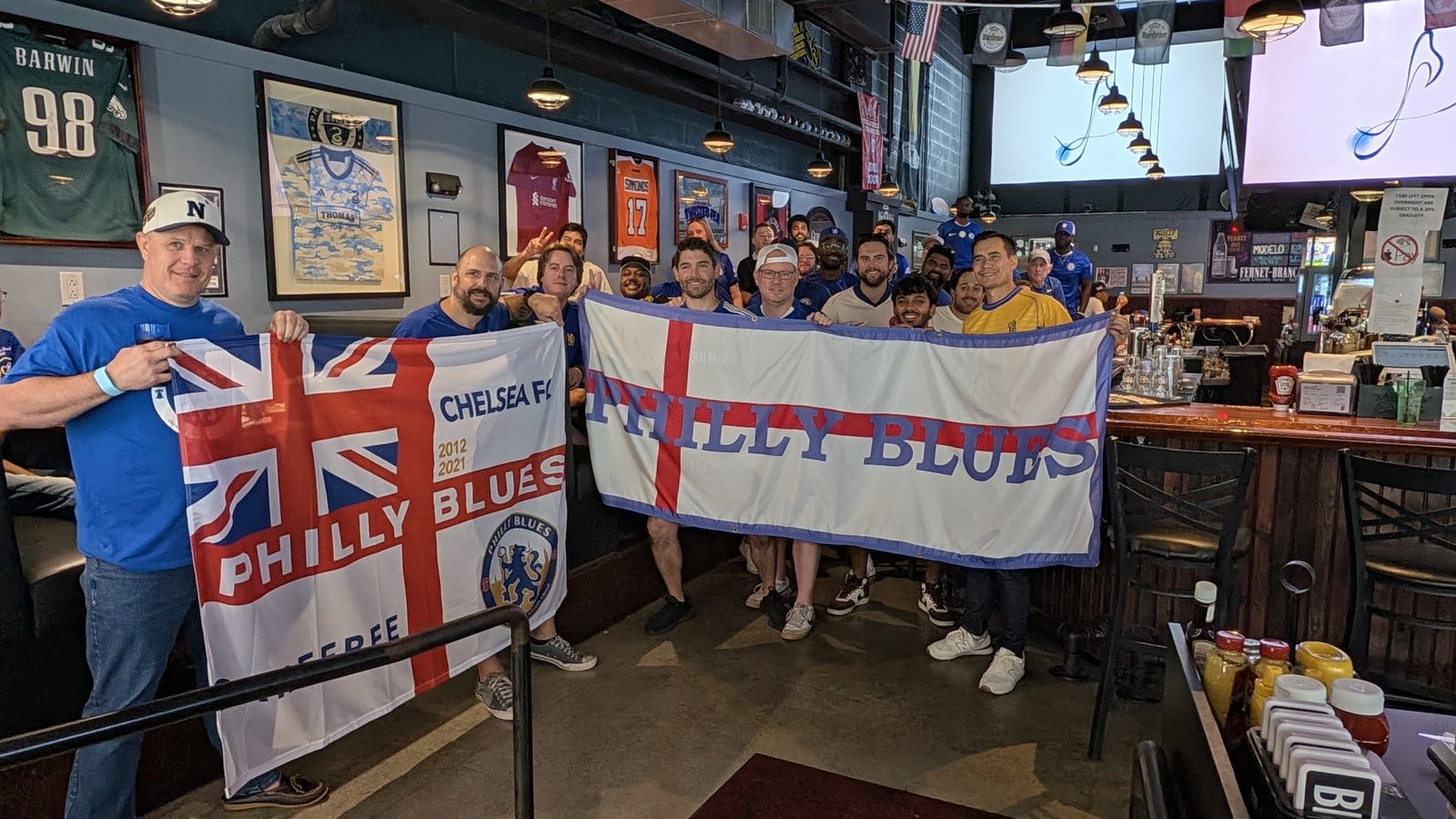 Around fifteen Philly Blues members crowded behind two banners at the bar — a Union Jack Philly Blues flag and a St George's cross Philly Blues flag.